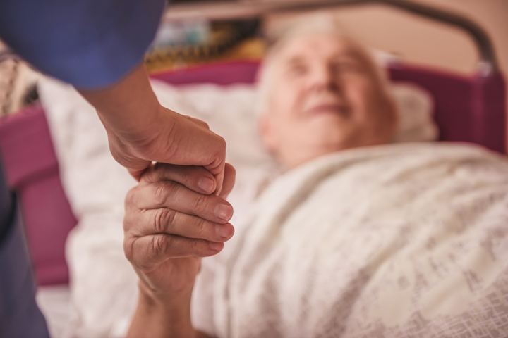 Pflegekraft haelt die Hand einer aelteren Frau im Krankenbett