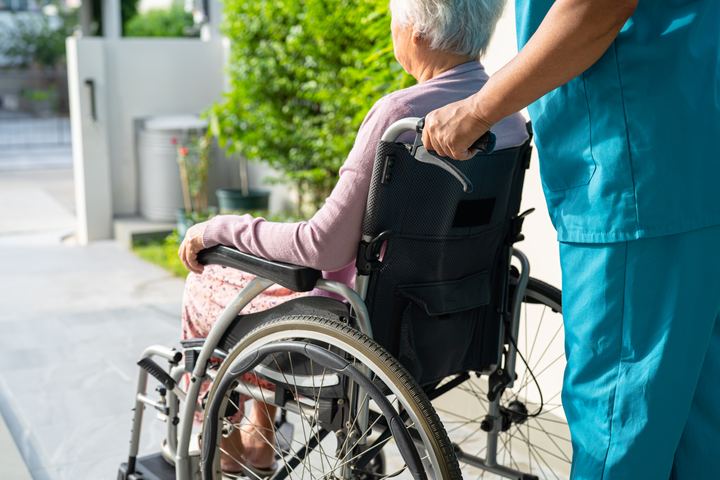 Pflegekraft schiebt eine ältere Dame im Rollstuhl